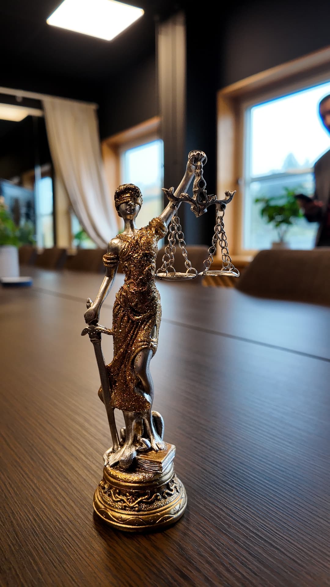 Justitias statyett med vågskål och svärd på ett mötesbord, med fönster och grönska i bakgrunden